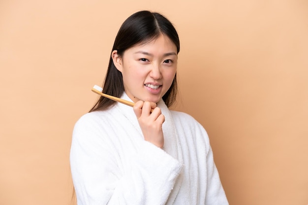Jovem chinesa isolada em fundo bege com escova de dentes e expressão feliz