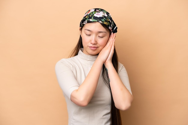 Jovem chinesa isolada em fundo bege fazendo gesto de sono em expressão adorável