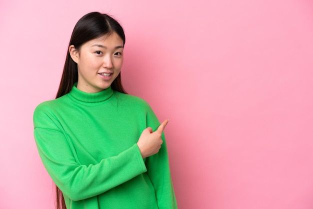 Jovem chinesa isolada em fundo rosa, apontando para trás