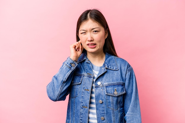 Jovem chinesa isolada em fundo rosa cobrindo orelhas com dedos estressados e desesperados por um ambiente barulhento