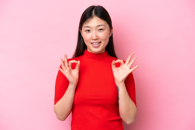 Jovem chinesa isolada em fundo rosa mostrando sinal de ok com as duas mãos