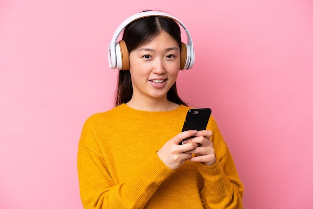 Jovem chinesa isolada em fundo rosa ouvindo música com um celular e olhando de frente