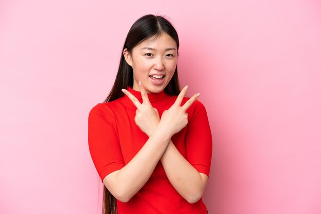 Jovem chinesa isolada em fundo rosa sorrindo e mostrando sinal de vitória
