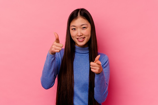 Jovem chinesa isolada em sorrisos alegres de fundo rosa, apontando para a frente.