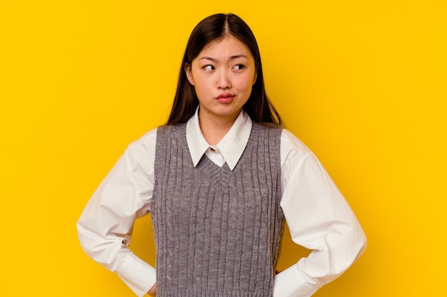 Jovem chinesa isolada em um fundo amarelo confusa, sente-se em dúvida e insegura.