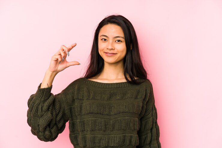 Foto jovem chinesa isolada em um fundo rosa segurando algo pequeno com os indicadores, sorrindo e confiante.