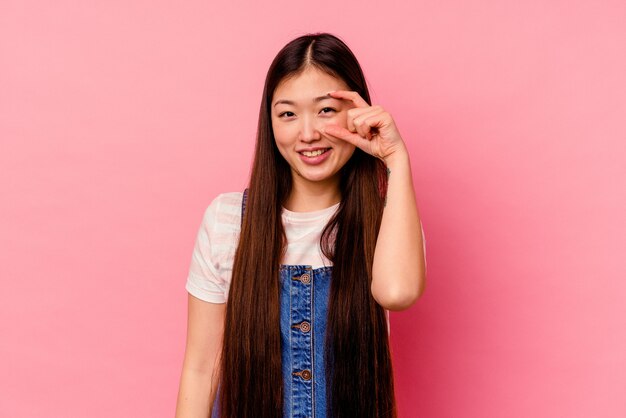 Jovem chinesa isolada na parede rosa mostrando sinal de aprovação sobre os olhos