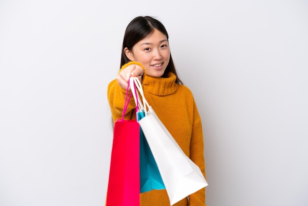 Jovem chinesa isolada no fundo branco segurando sacolas de compras e dando-as a alguém