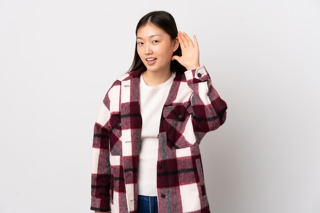 Jovem chinesa isolada ouvindo alguma coisa colocando a mão na orelha