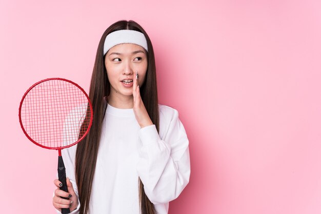 Jovem chinesa jogando badminton isolado está dizendo uma notícia secreta sobre a frenagem quente e olhando de lado