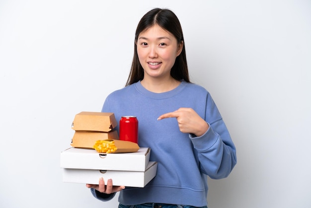 Jovem chinesa segurando fast-food isolado no fundo branco, apontando para o lado para apresentar um produto