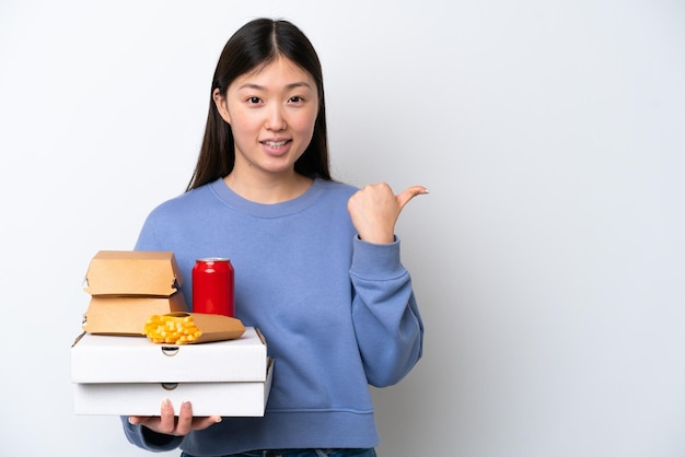 Jovem chinesa segurando fast-food isolado no fundo branco, apontando para o lado para apresentar um produto