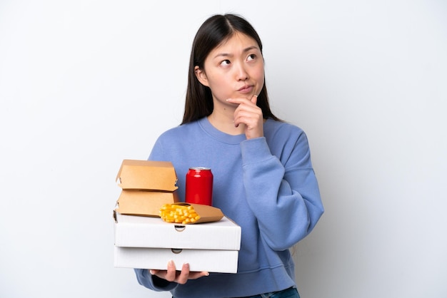 Jovem chinesa segurando fast-food isolado no fundo branco com dúvidas