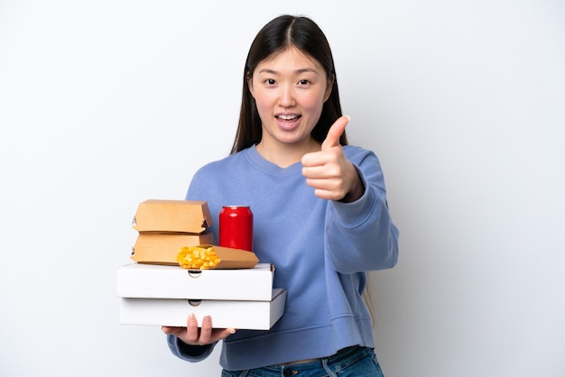 Jovem chinesa segurando fast-food isolado no fundo branco com polegares para cima porque algo bom aconteceu