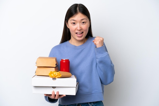 Jovem chinesa segurando fast food isolado no fundo branco comemorando uma vitória na posição de vencedor