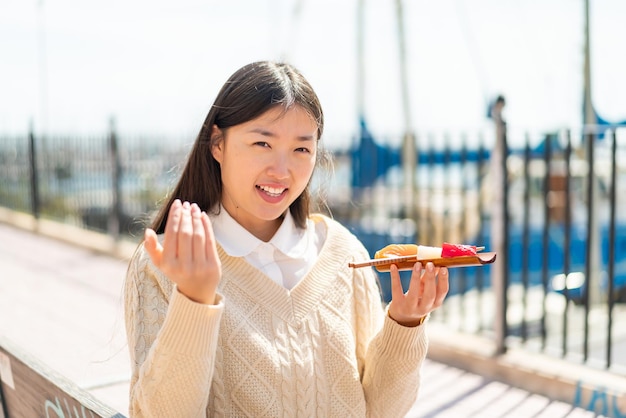 Jovem chinesa segurando sashimi ao ar livre convidando para vir com a mão feliz que você veio