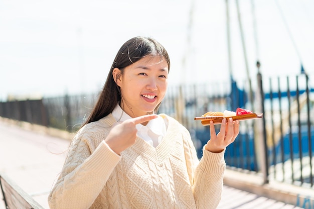 Jovem chinesa segurando sashimi ao ar livre e apontando-o