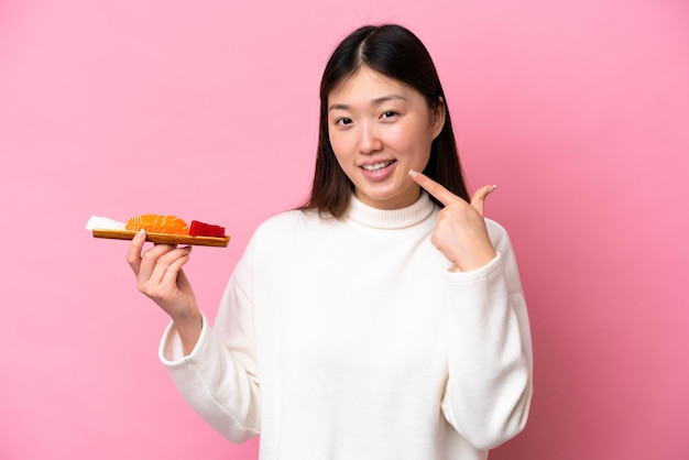 Jovem chinesa segurando sashimi isolado em fundo rosa dando um polegar para cima gesto