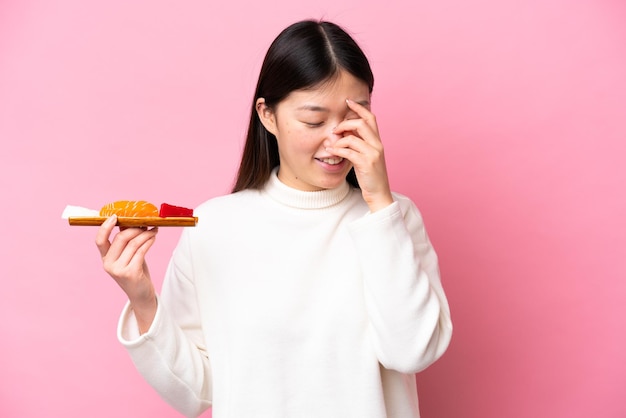 Jovem chinesa segurando sashimi isolado no fundo rosa rindo