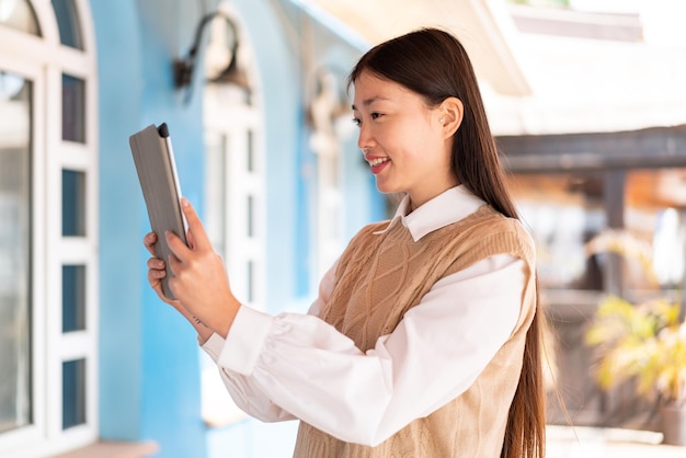 Jovem chinesa segurando um tablet ao ar livre com expressão feliz