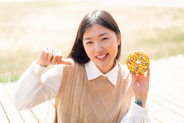 Jovem chinesa segurando uma rosquinha ao ar livre orgulhosa e satisfeita