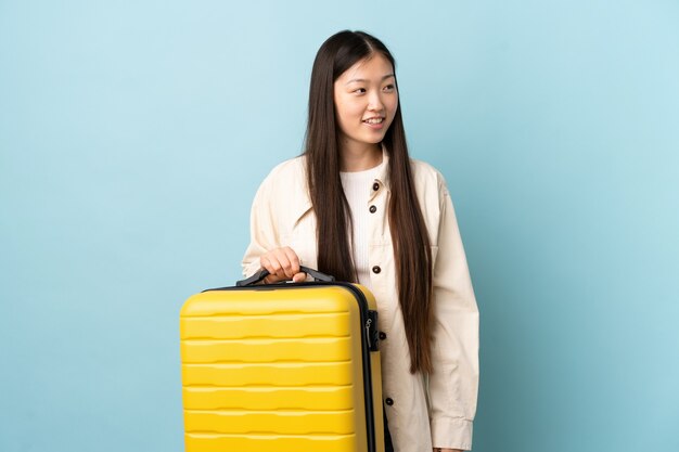 Jovem chinesa sobre uma parede isolada em férias com uma mala de viagem