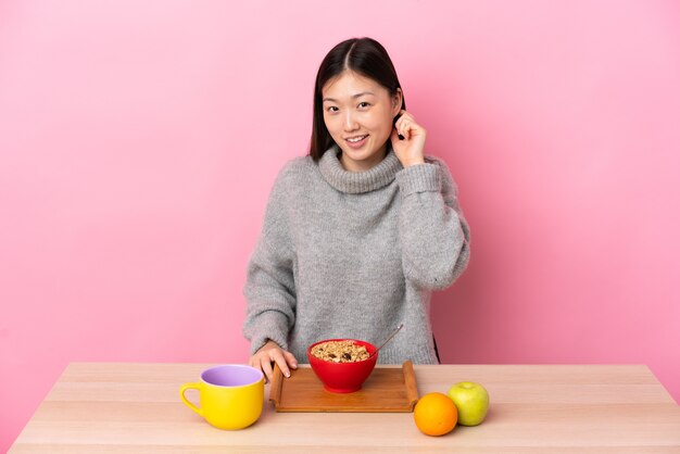 Jovem chinesa tomando café da manhã em uma mesa rindo