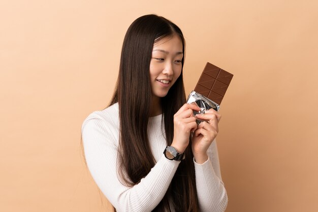 Jovem chinesa tomando um comprimido de chocolate e feliz