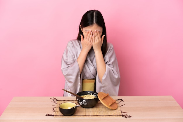 Jovem chinesa vestindo quimono e comendo macarrão com expressão cansada e doente
