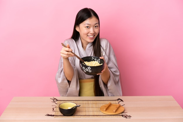 Jovem chinesa vestindo quimono e comendo macarrão em uma mesa rosa