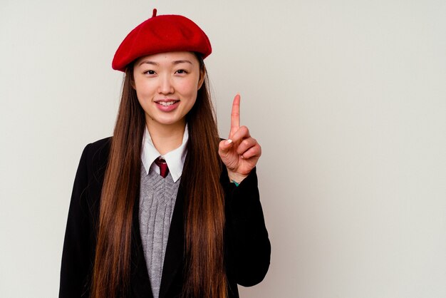 Jovem chinesa vestindo um uniforme escolar isolado na parede branca, mostrando o número um com o dedo
