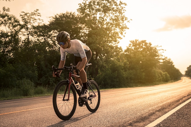 Jovem ciclista andando de bicicleta em uma estrada aberta ao pôr do sol