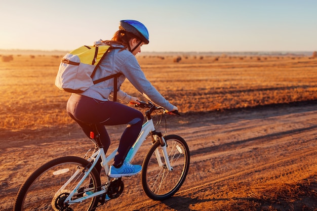Jovem ciclista andando no campo de outono com montes de feno ao pôr do sol. Mulher com mochila viajando de bicicleta. Estilo de vida saudável.