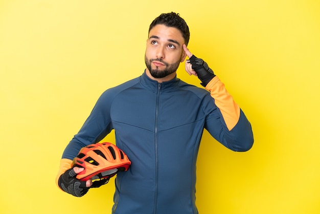 Foto jovem ciclista árabe isolado em fundo amarelo, tendo dúvidas e pensando