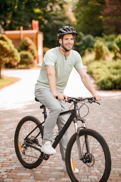 Jovem ciclista caucasiano sorridente e satisfeito com um capacete de segurança andando de bicicleta no parque