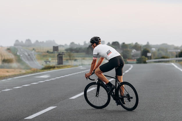 Jovem ciclista com corpo atlético vestido com roupas esportivas, correndo na estrada durante o dia de verão