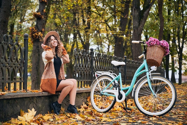 Foto jovem ciclista descansando no meio-fio perto de bicicleta no outono