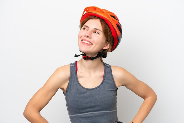 Jovem ciclista inglesa isolada em fundo branco posando com braços no quadril e sorrindo