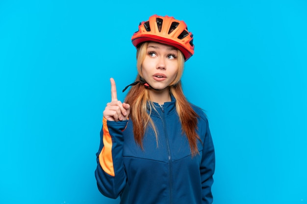 Jovem ciclista isolada em um fundo azul pensando em uma ideia apontando o dedo para cima