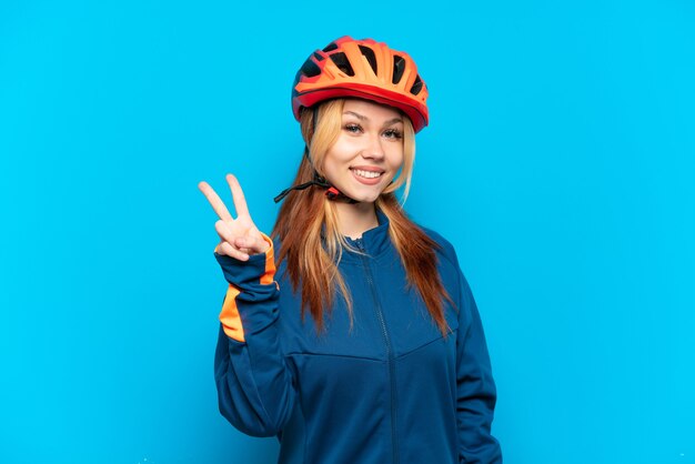 Jovem ciclista isolada em um fundo azul sorrindo e mostrando sinal de vitória