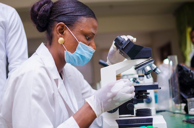 Jovem cientista africana olhando através de um microscópio no laboratório sobre a vacina em que está trabalhando.