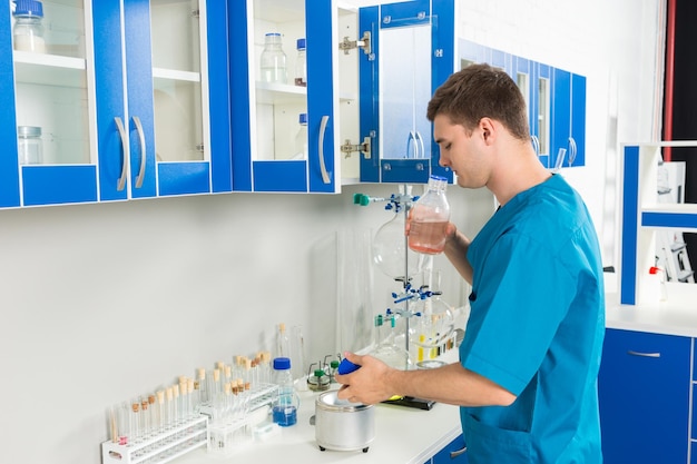 Jovem cientista de uniforme está cheirando uma garrafa com substância química em um laboratório. conceito de saúde e biotecnologia