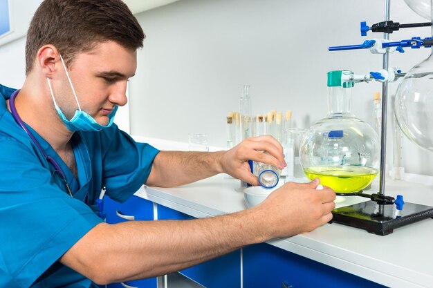 Foto jovem cientista de uniforme usando uma máscara está trabalhando com frascos de química e fazendo algumas pesquisas em um laboratório. conceito de saúde e biotecnologia