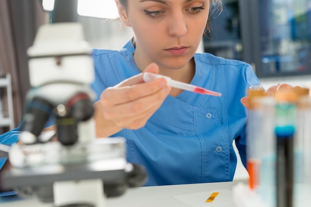 Jovem cientista feminina concentrada de uniforme, trabalhando em algumas pesquisas em um laboratório. Conceito de saúde e biotecnologia