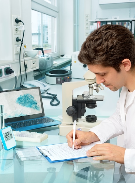 Jovem cientista masculino ou tecnologia faz anotações no laboratório de histopatologia