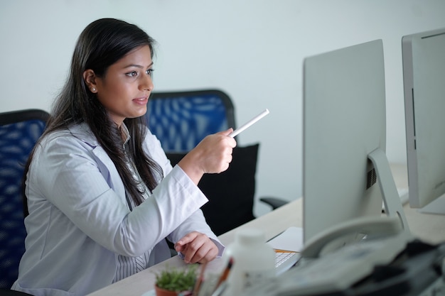 Jovem cientista ou trabalhador de laboratório médico apontando para a tela do computador ao analisar gráficos ou dados de pesquisa