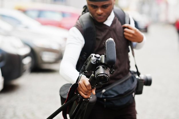 Jovem cinegrafista afro-americano profissional segurando uma câmera profissional com equipamento tripé Pro cinegrafista afro vestindo duraq preto fazendo vídeos