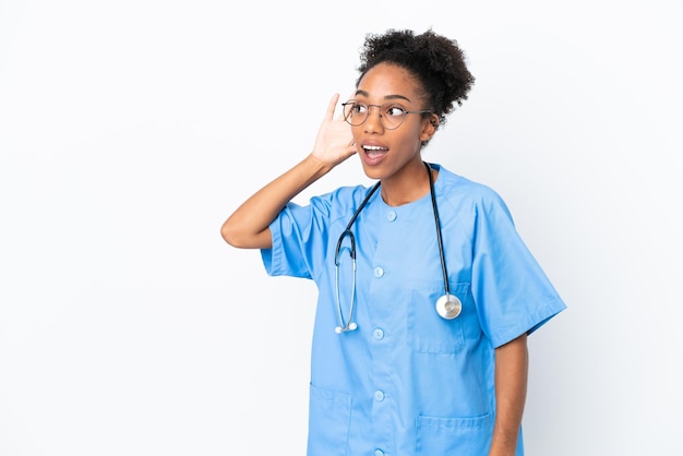 Jovem cirurgiã médica afro-americana isolada em fundo branco ouvindo algo colocando a mão na orelha