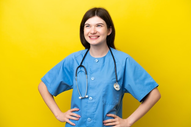 Jovem cirurgiã médica mulher russa isolada em fundo amarelo posando com braços no quadril e sorrindo