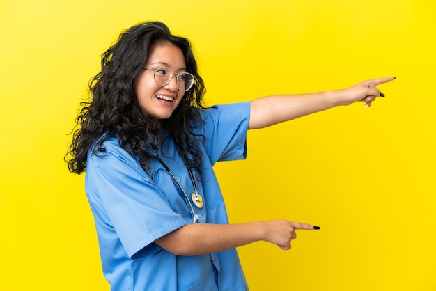 Jovem cirurgiã mulher asiática isolada em fundo amarelo apontando o dedo para o lado e apresentando um produto